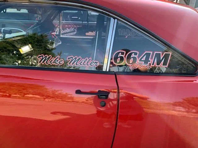 A red car with a sticker on the window that says mike muller