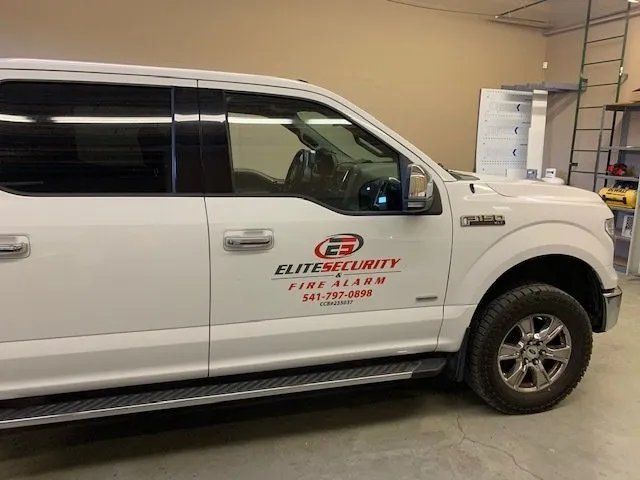 A white truck with a sticker on the side that says elite security firm alarm