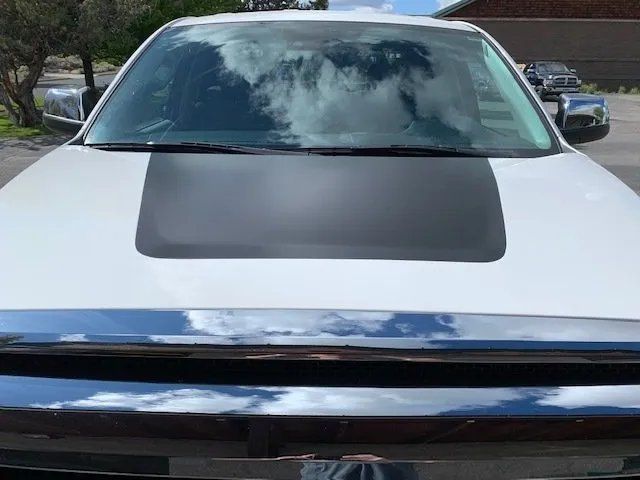 A white truck with a black hood stripe is parked in a driveway.