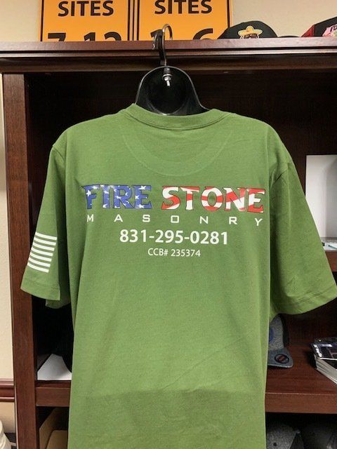 A green firestone masonry t-shirt is hanging on a hanger