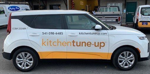 A white and yellow car with the words kitchen tune up on the side is parked in a parking lot.