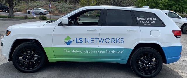 A white jeep with ls networks written on the side is parked in a parking lot.
