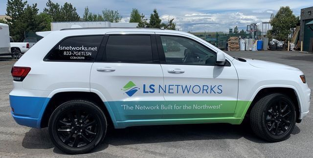 A white suv with ls networks written on the side is parked in a parking lot.