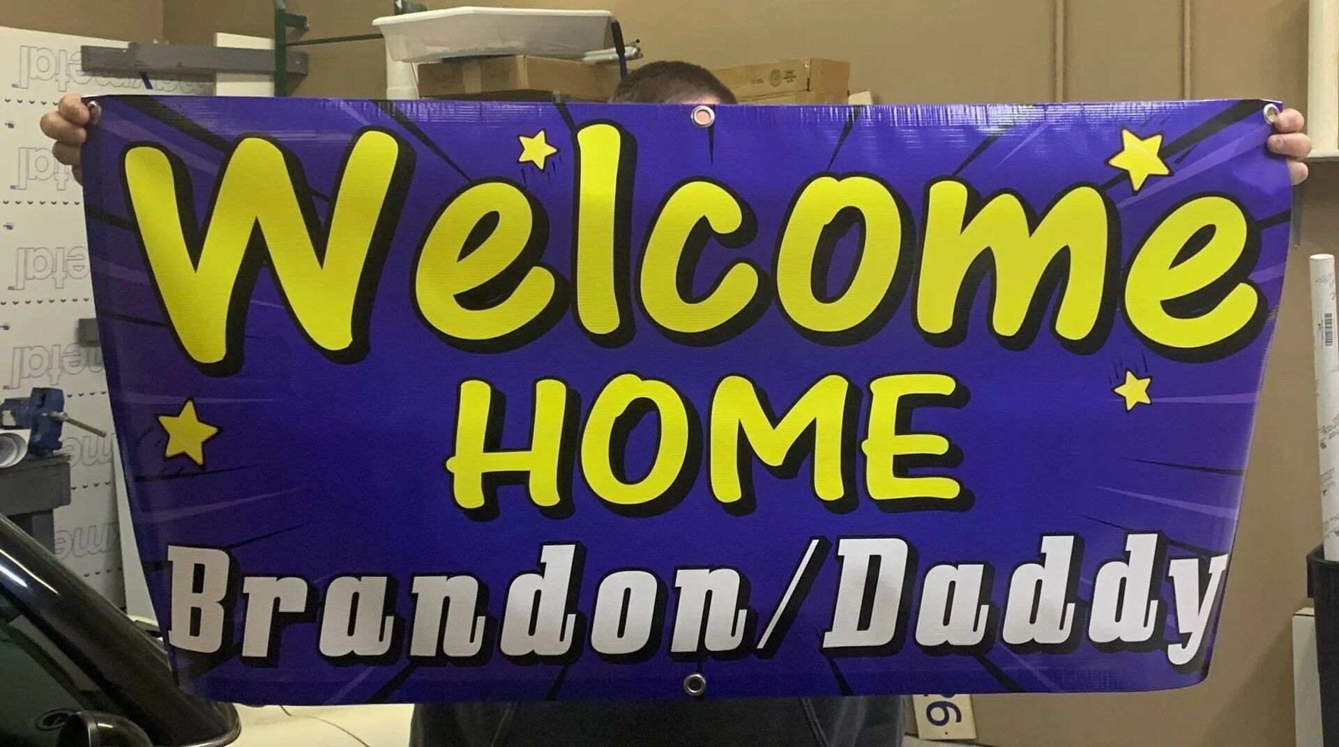 A man is holding a welcome home banner for brandon and daddy