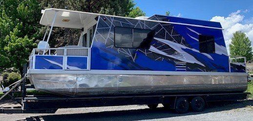 A blue and white pontoon boat is parked on a trailer.