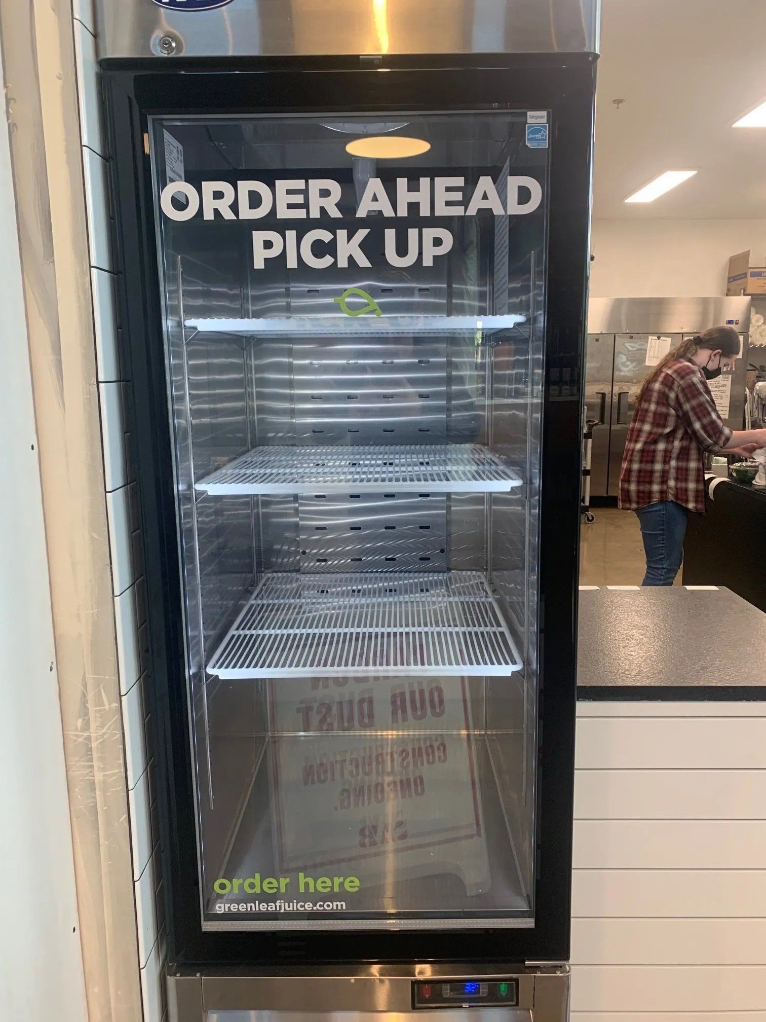 A man is standing in front of a refrigerator that says `` order ahead pick up ''.