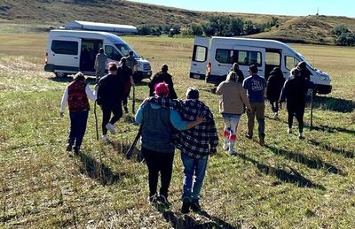 A group of people are walking in a field with vans in the background.