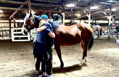 A woman is hugging a brown horse in a barn.