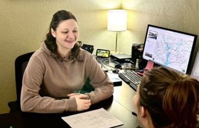 Two women are sitting at a desk in front of a computer.