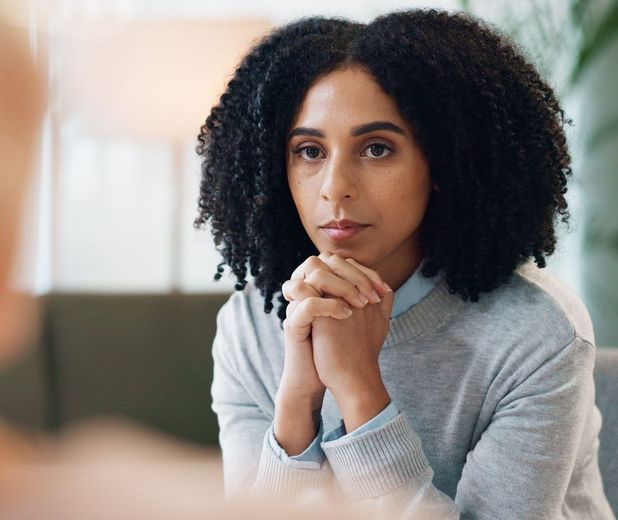 A woman with curly hair is sitting on a couch with her hands folded.