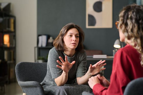 A woman is sitting in a chair talking to another woman.