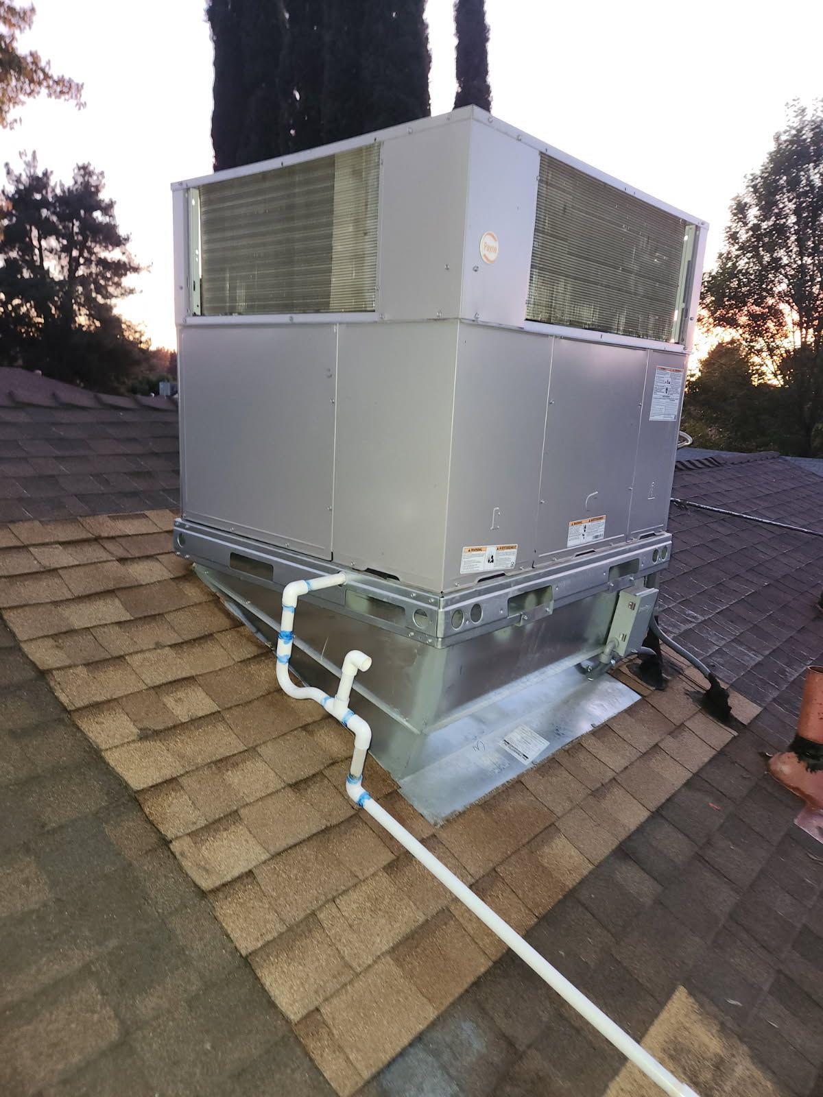 White air conditioning unit mounted on a building exterior, near green plants.