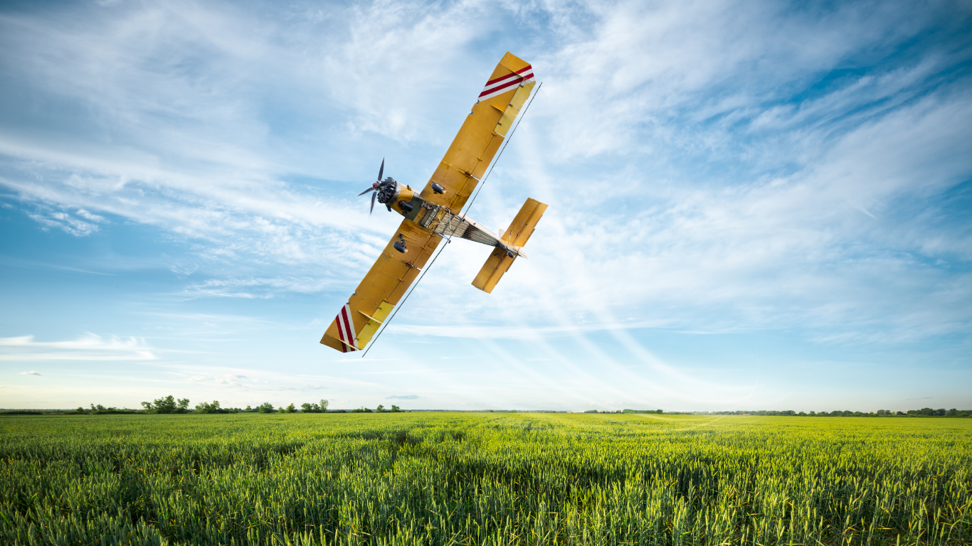 a yellow airplane is flying over a green field .