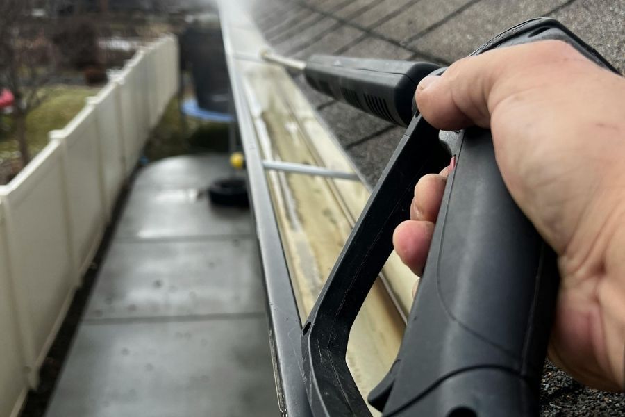 Worker clearing debris from clogged rain gutter on residential property