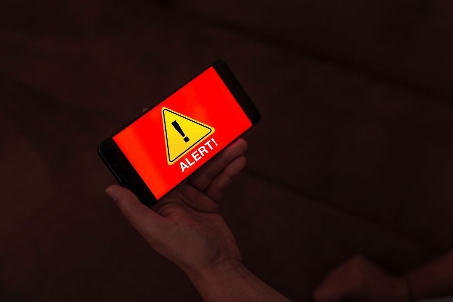 Hand holding a smartphone displaying a red emergency alert warning message during a wildfire event