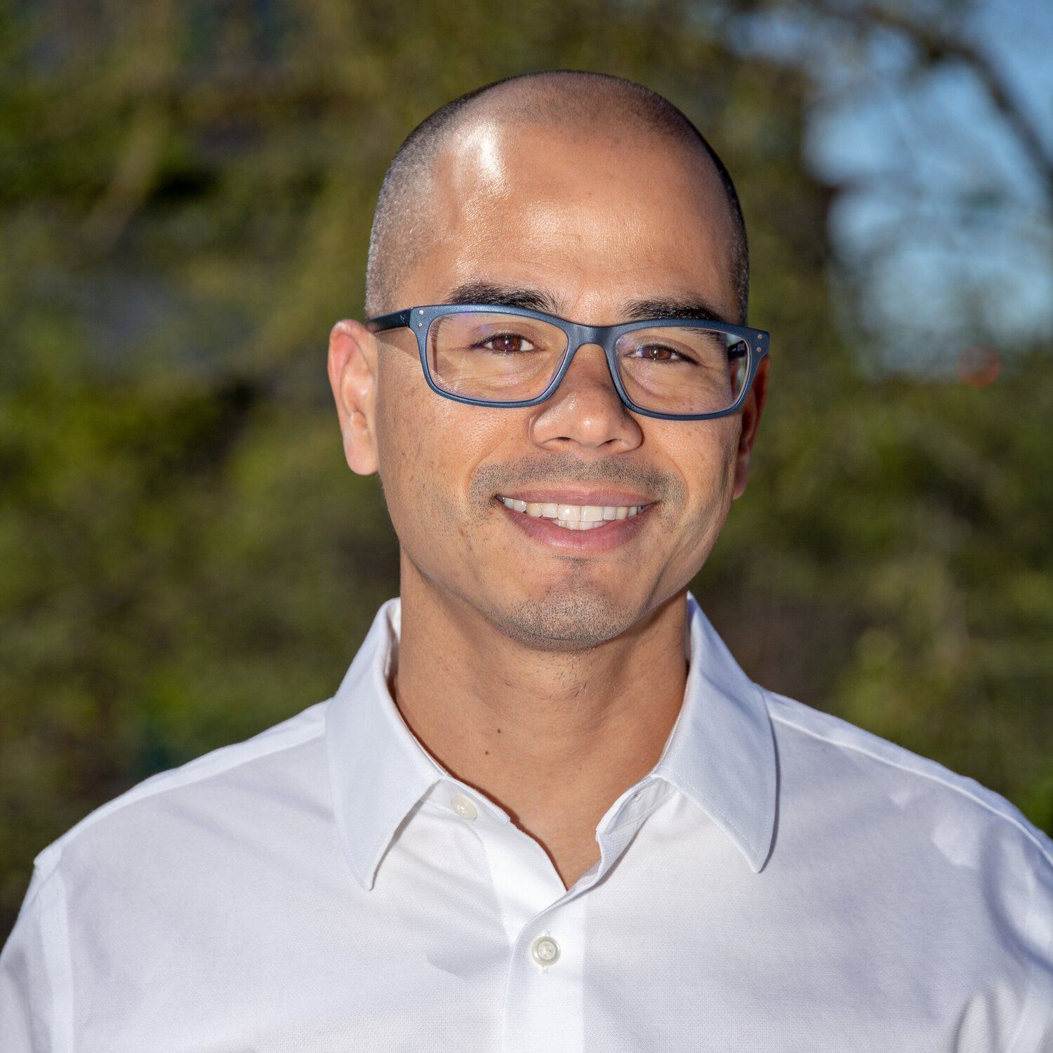 A man wearing glasses and a white shirt is smiling for the camera.
