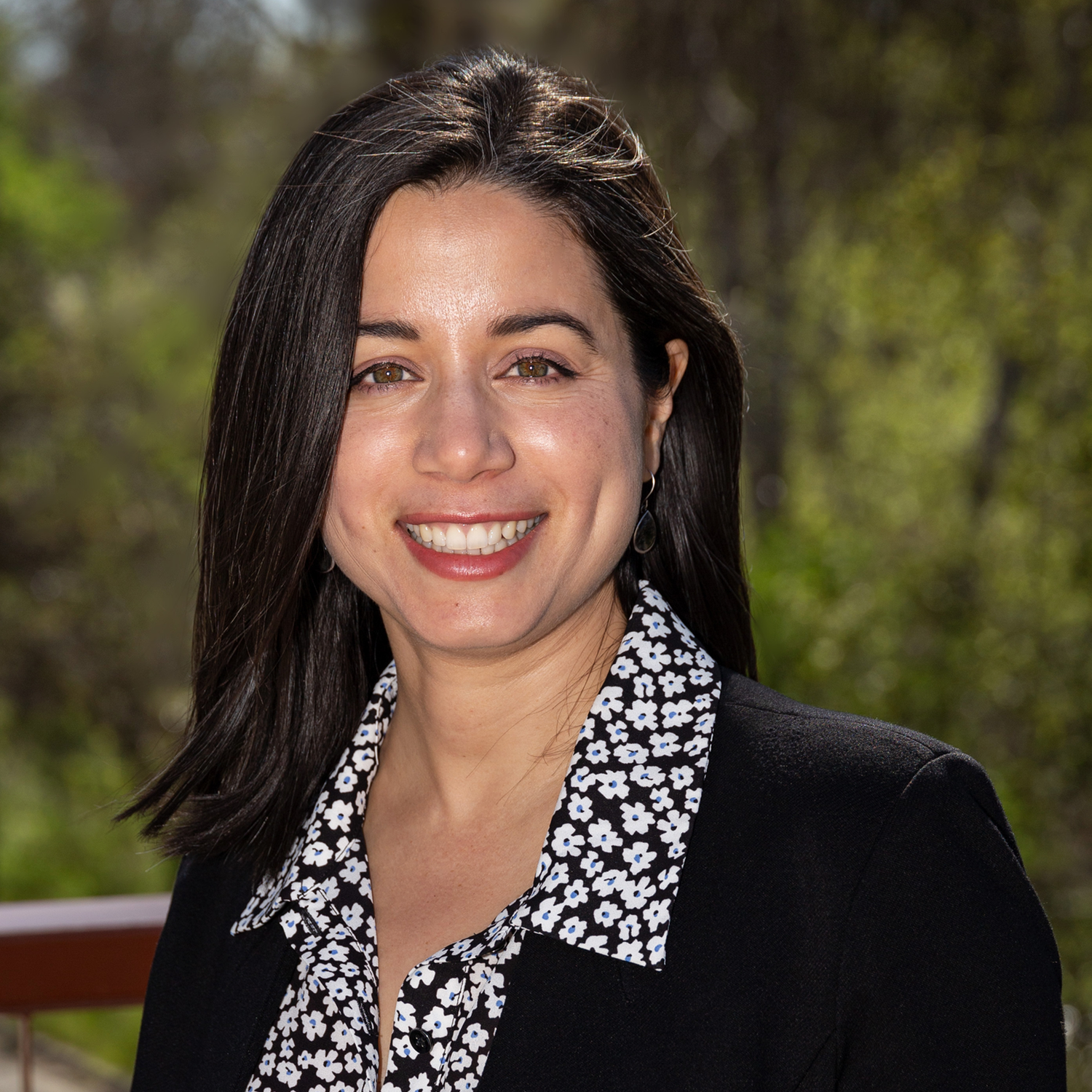 A woman wearing a black jacket and a floral shirt is smiling for the camera.