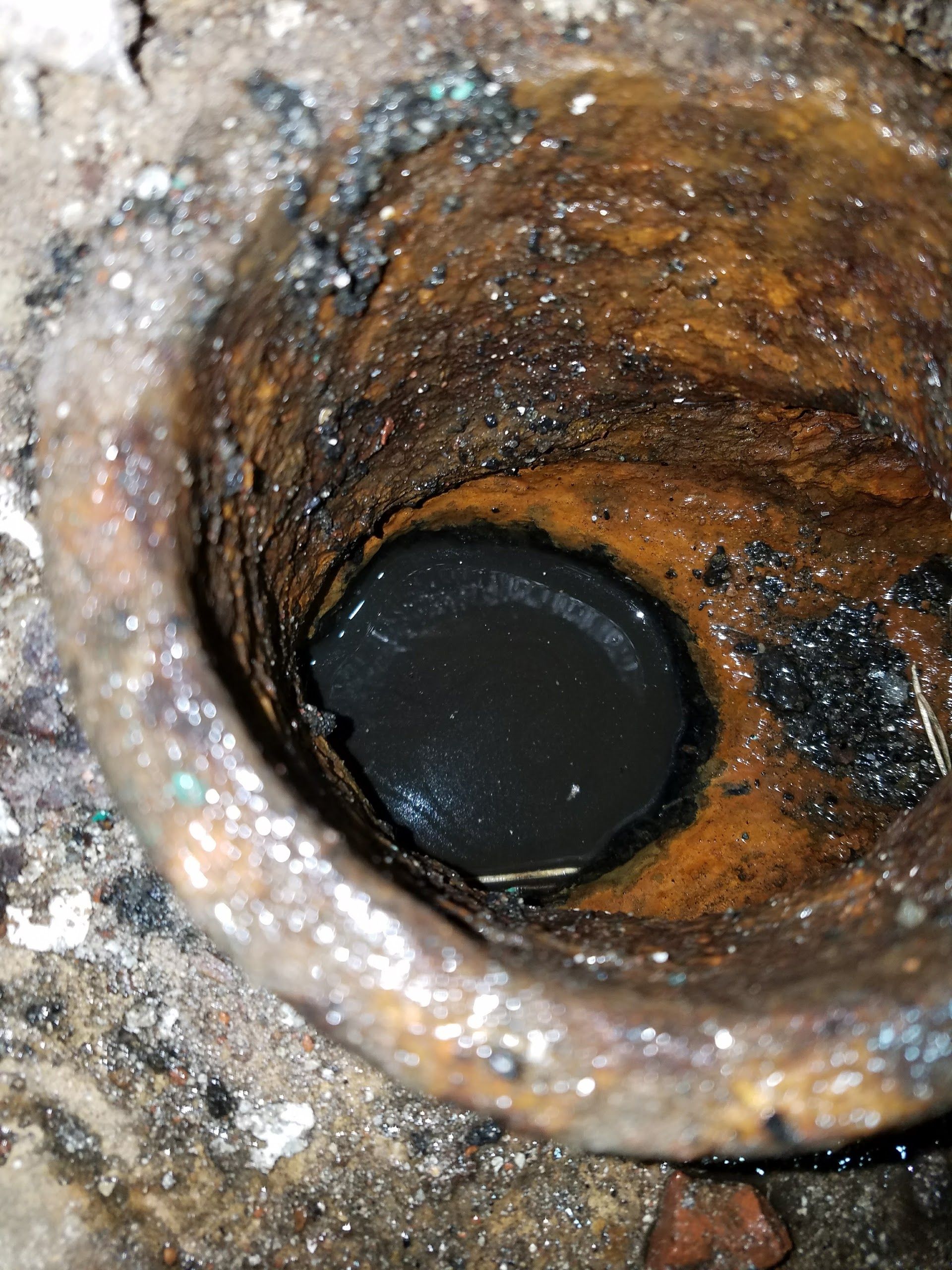 Corroded drain pipe filled with dark, stagnant water. Rusty interior with black debris.