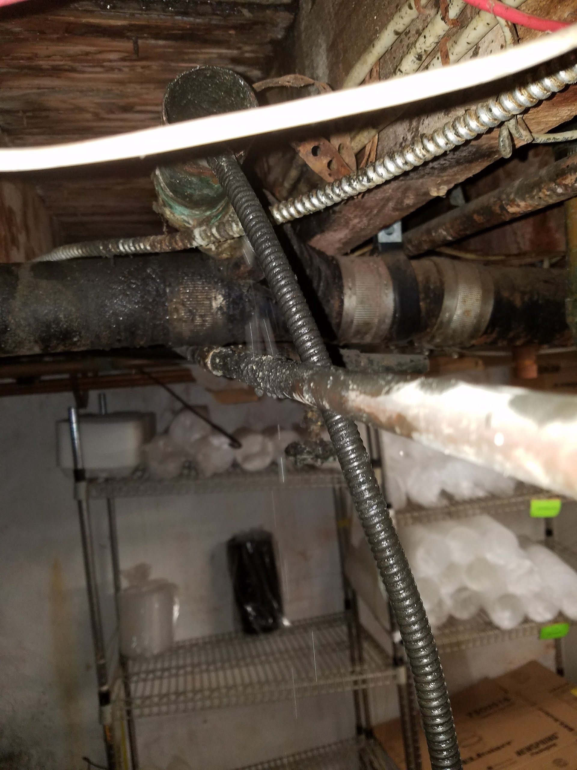 Leaking pipe under a ceiling with electrical wiring, showing water droplets and rust.