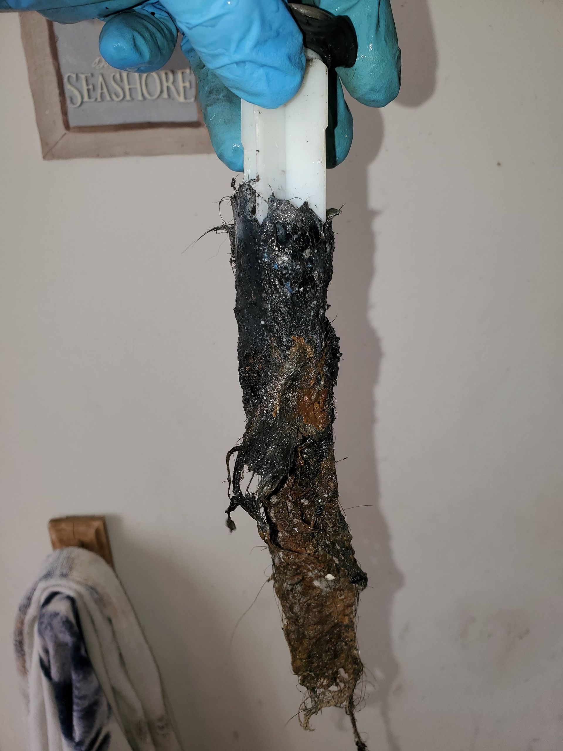 A gloved hand holds a clogged, dirty toilet fill valve.