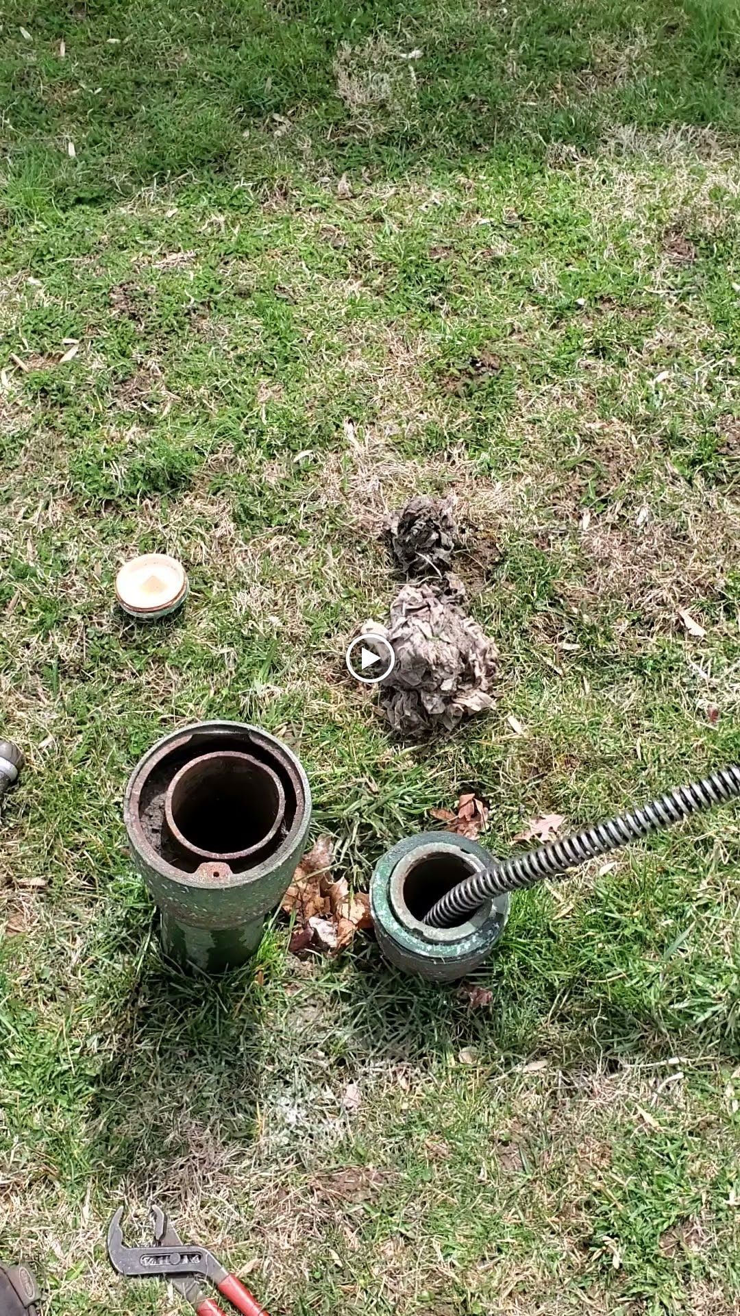 Well pipe components in grass, a drain snake being used, and tools.