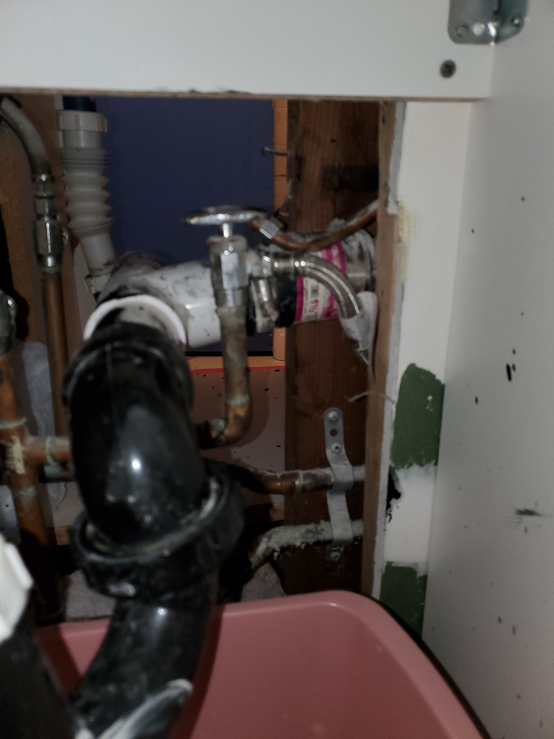 Plumbing pipes under a sink. Black drainpipes, copper water lines, and a shut-off valve are visible.