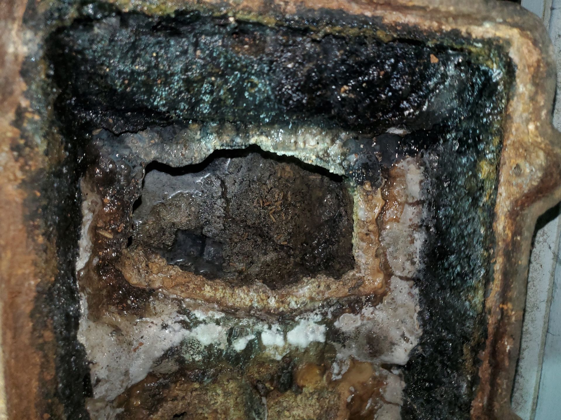 Inside of a rusted cast iron stove with a dark, melted substance and crumbling interior.