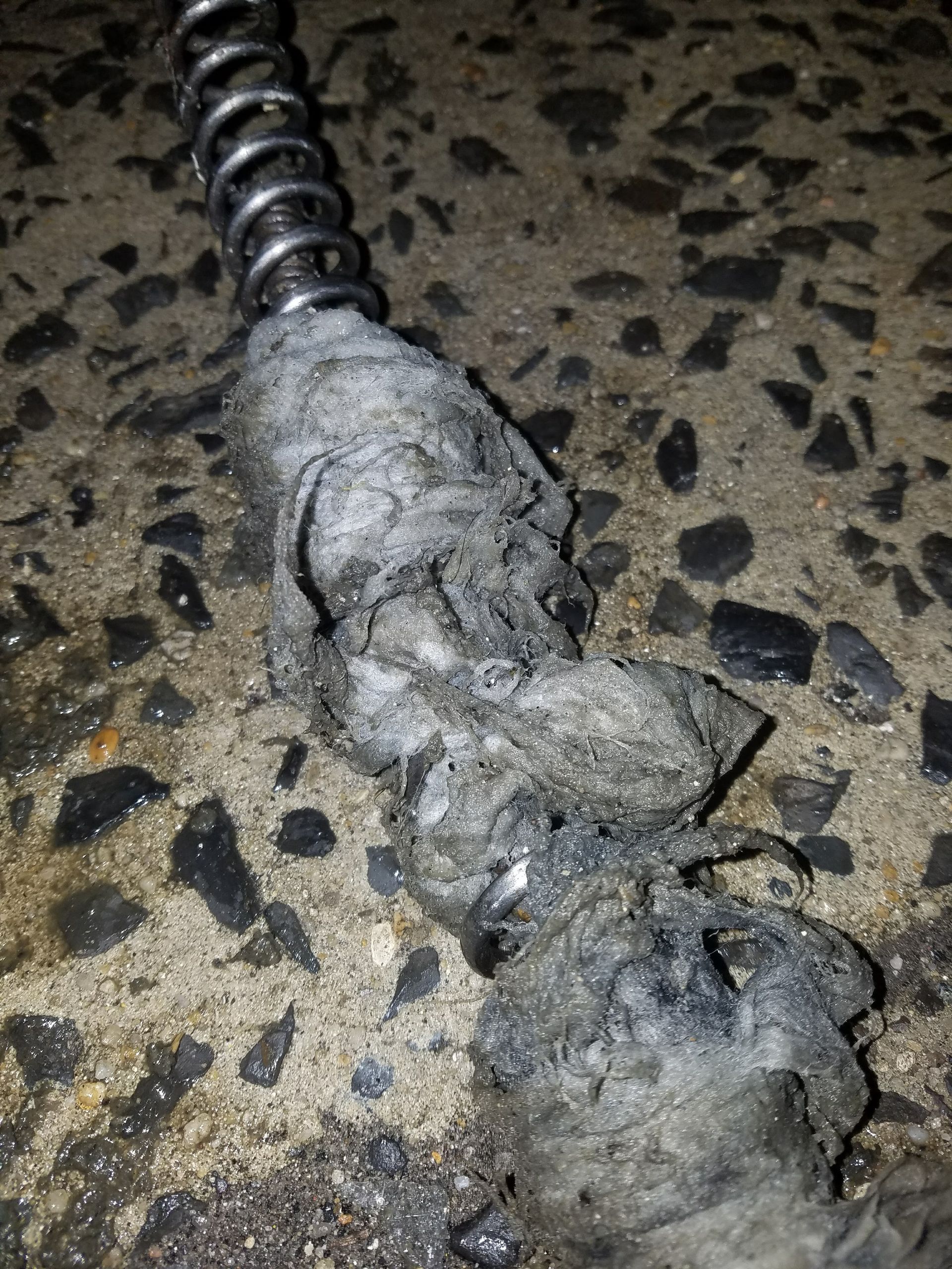 Damaged electrical cable, charred insulation, on concrete. Metal coil visible.