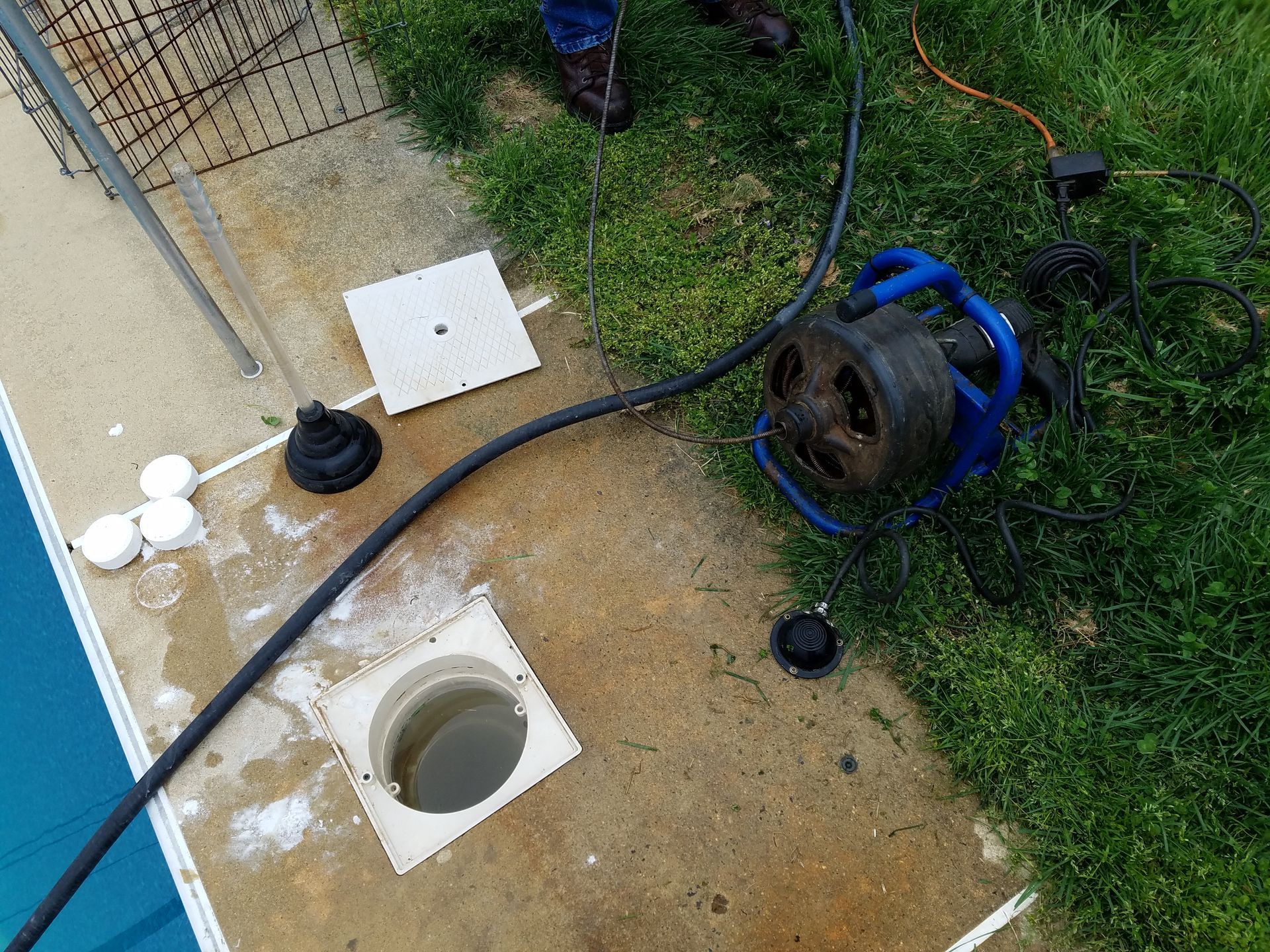 Poolside scene with a drain, pump, and equipment on concrete next to a pool and grass.