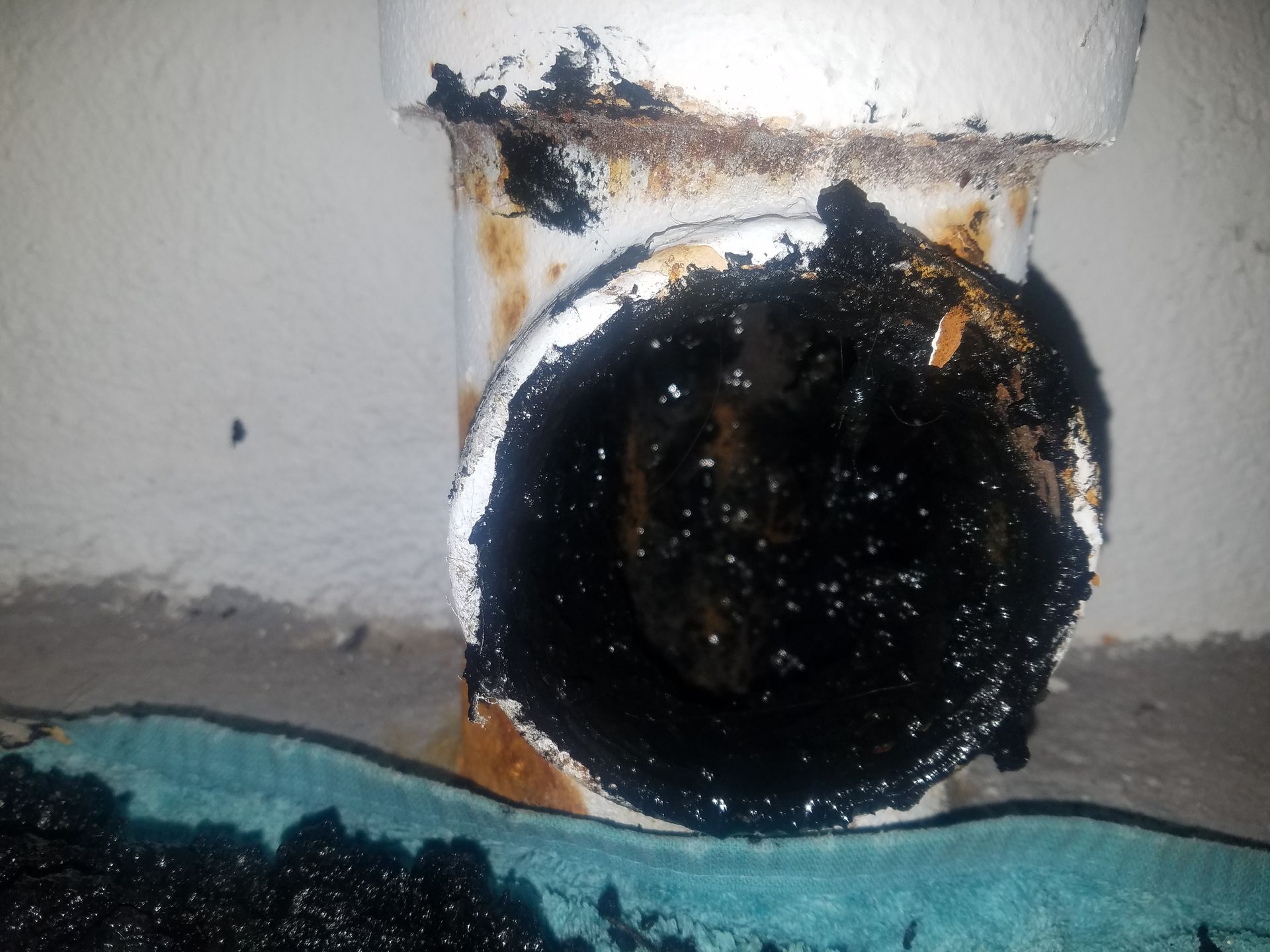 Black, oily residue surrounds a white pipe fitting where it connects to the wall.