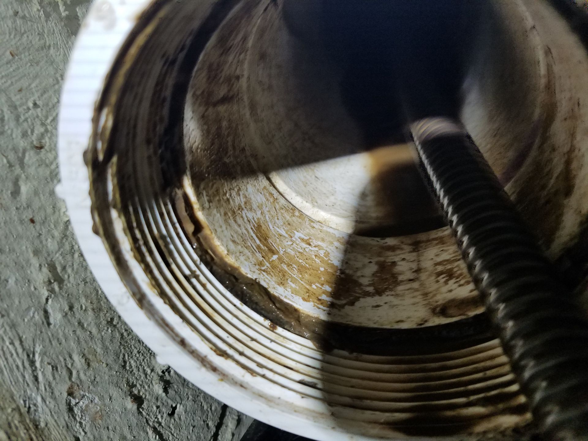 Inside view of a white PVC pipe with dirt and a threaded rod.