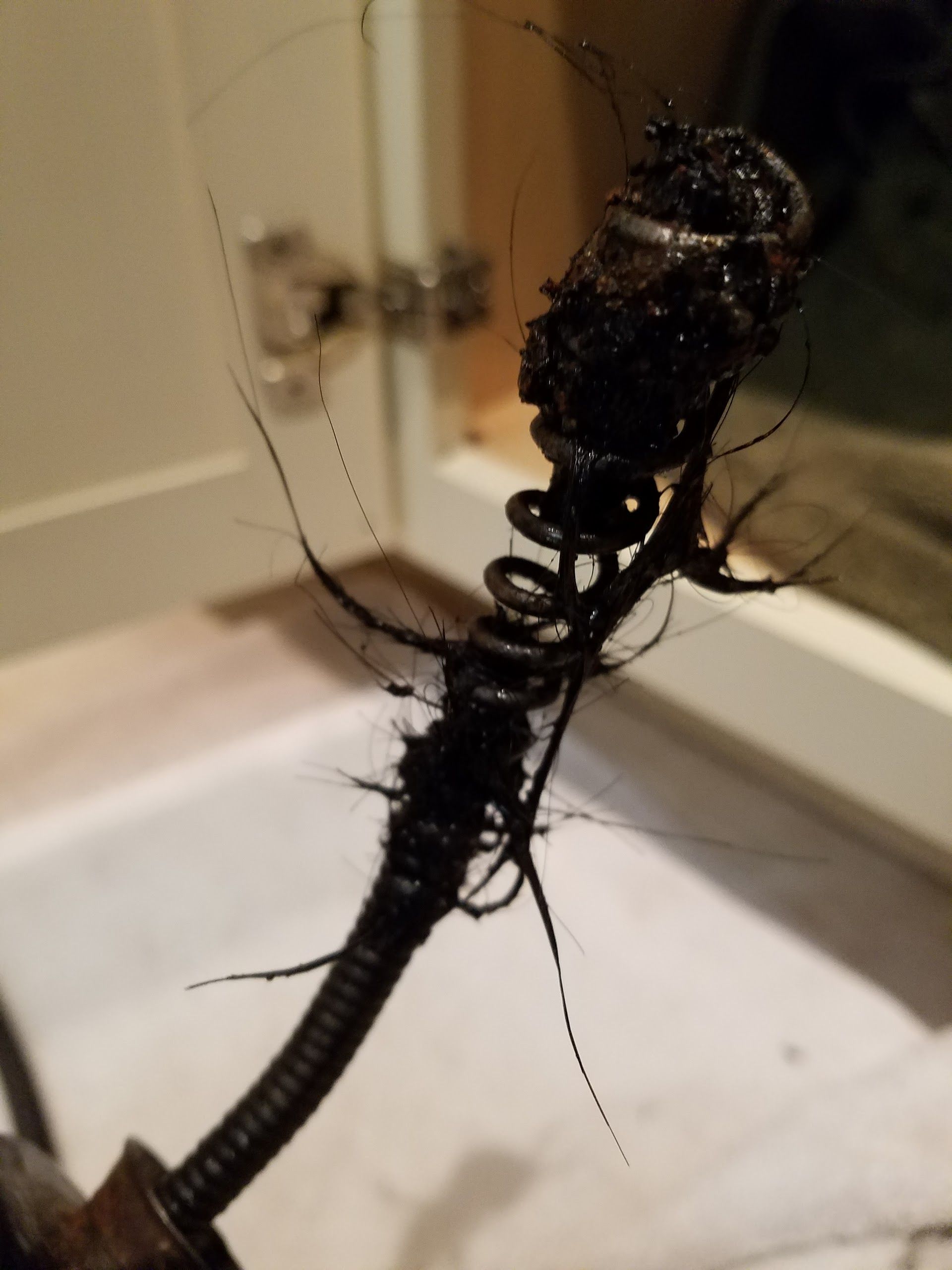 A drain snake covered in a black, clotted mass of hair and grime is held near a sink.