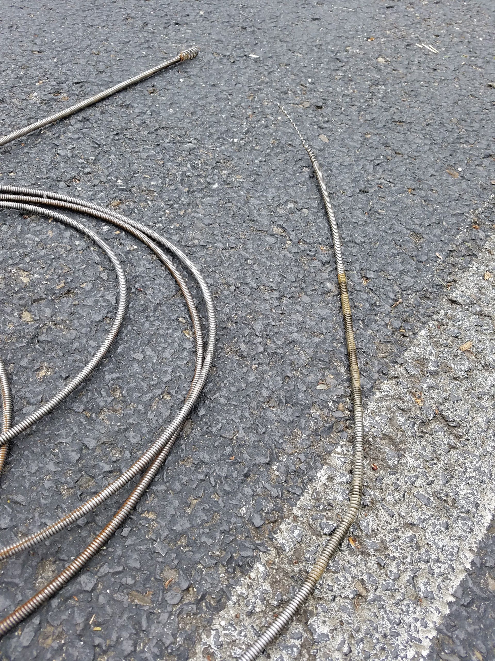 Coiled, silver-colored cable on asphalt next to a white line.