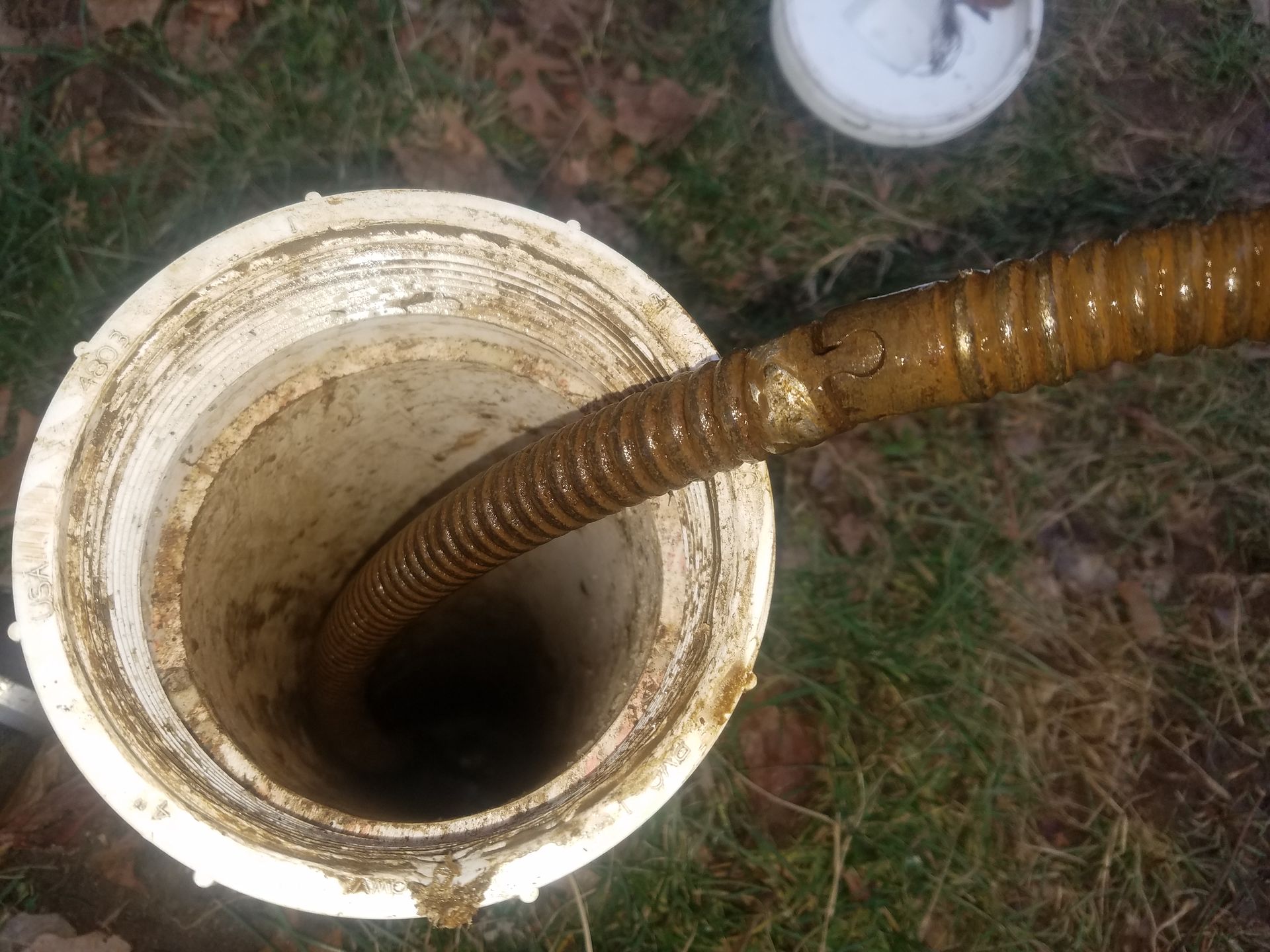 A well with a brown, corrugated pipe inside, surrounded by dirt and grass.