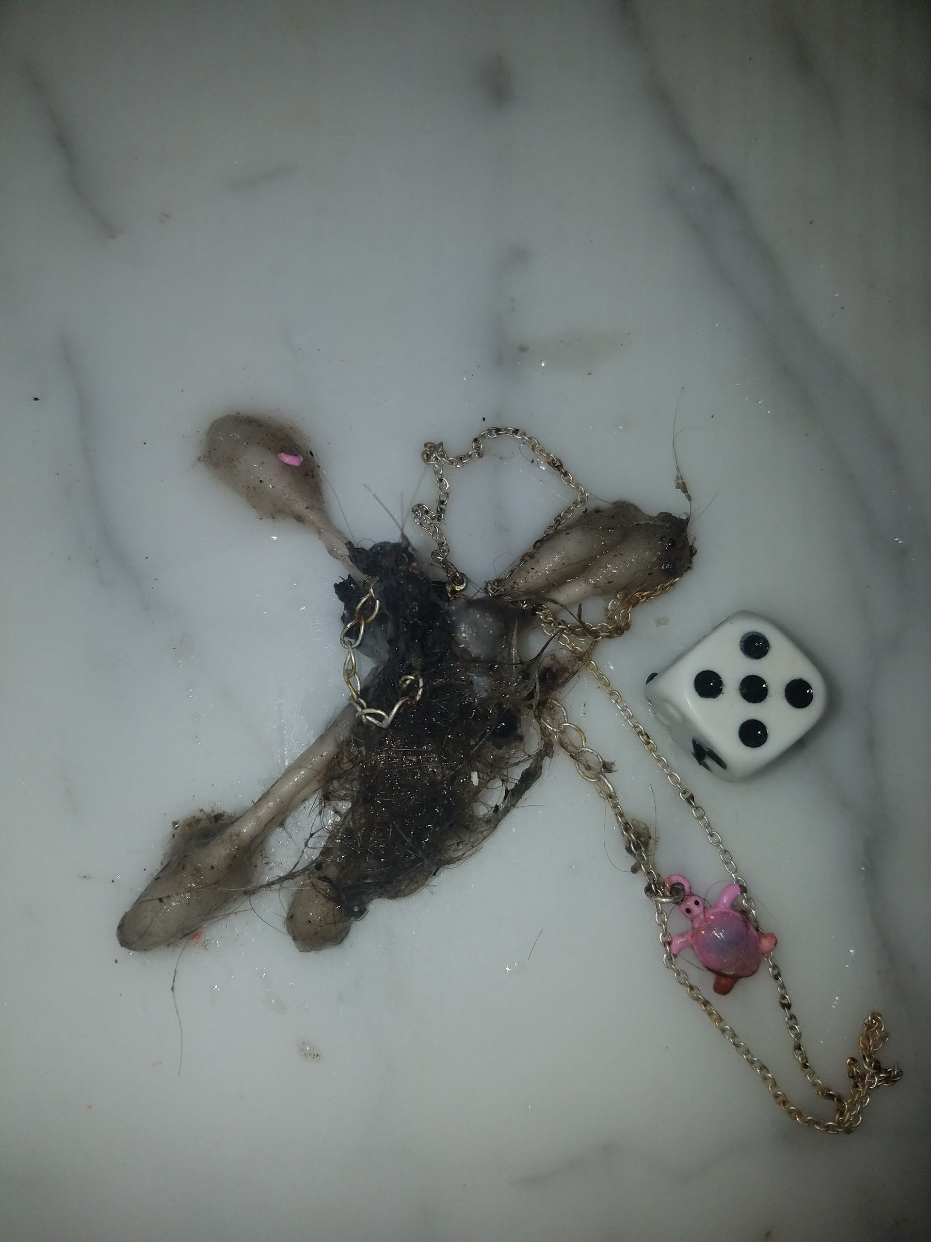 Spoiled food and jewelry on a white, marble surface next to a die showing five dots.