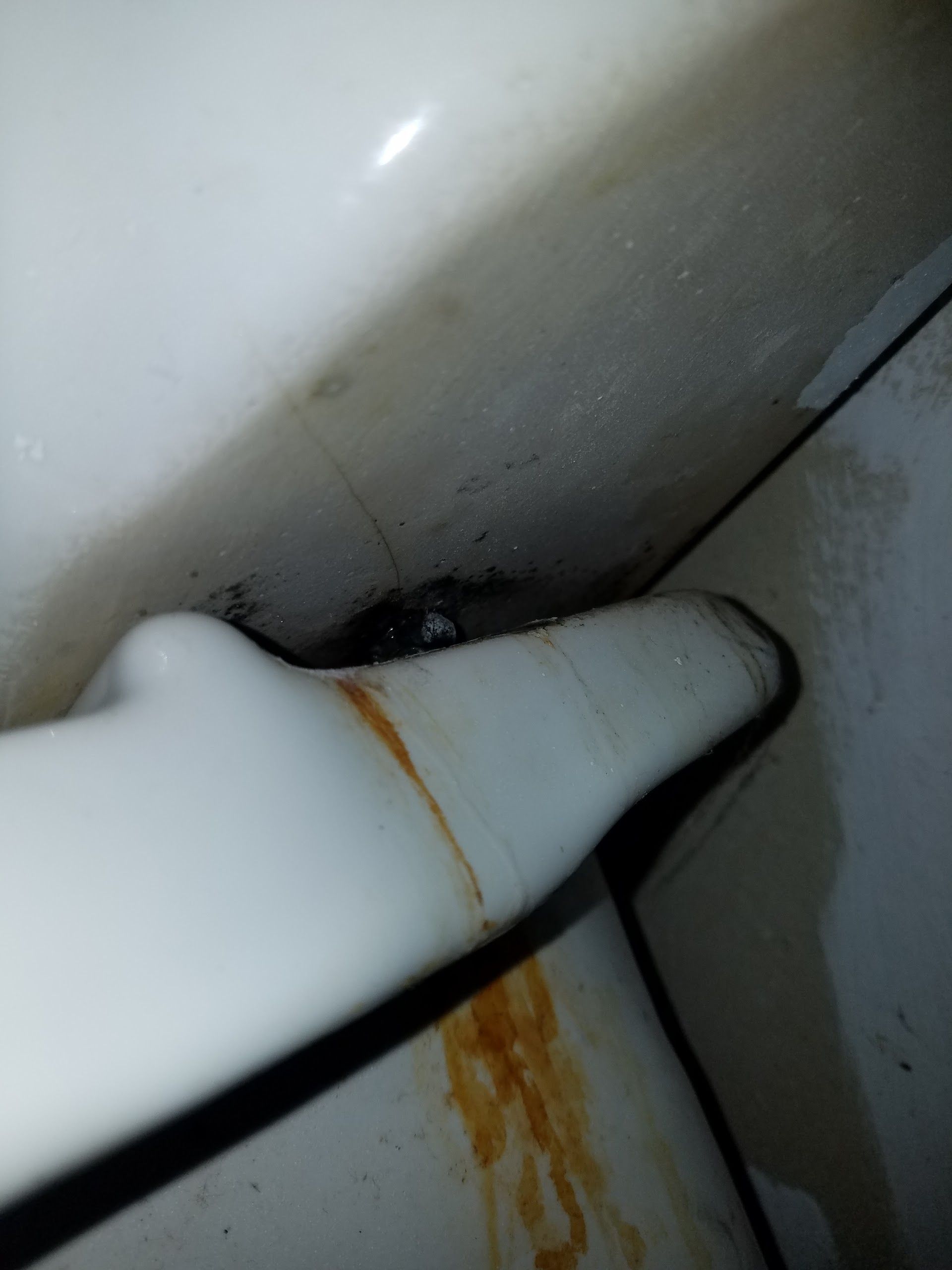 Close-up of a white porcelain toilet tank lever with dark staining and discoloration in the surrounding area.