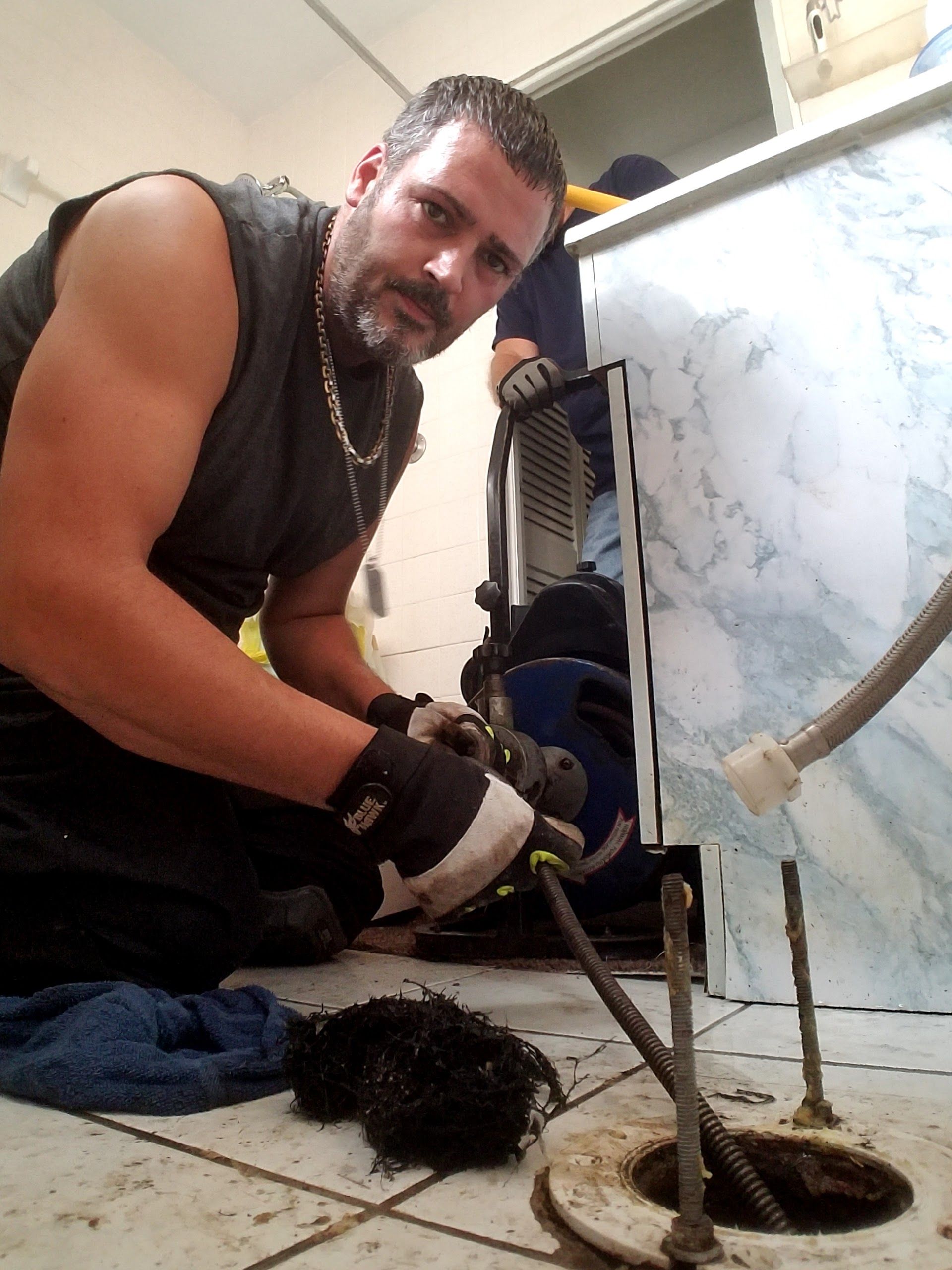 Man using a drain auger on a floor drain, inside a utility room.