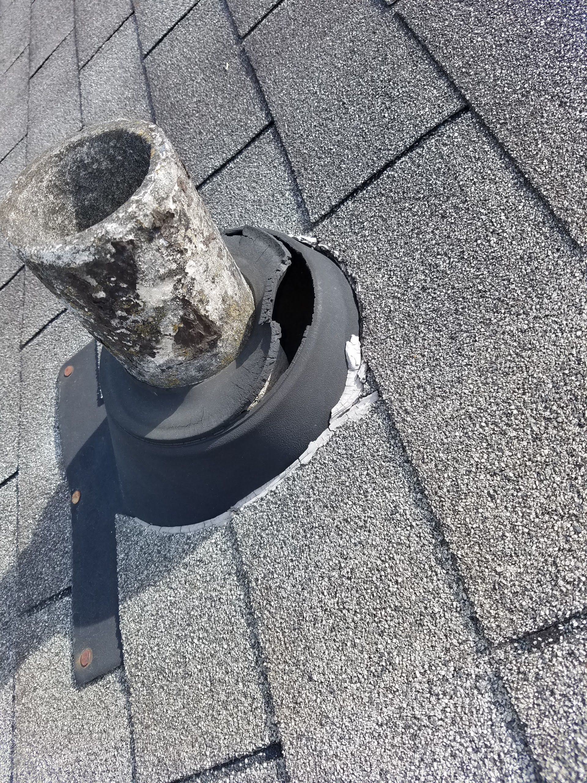 Damaged roof flashing around a vent pipe on a shingled roof.