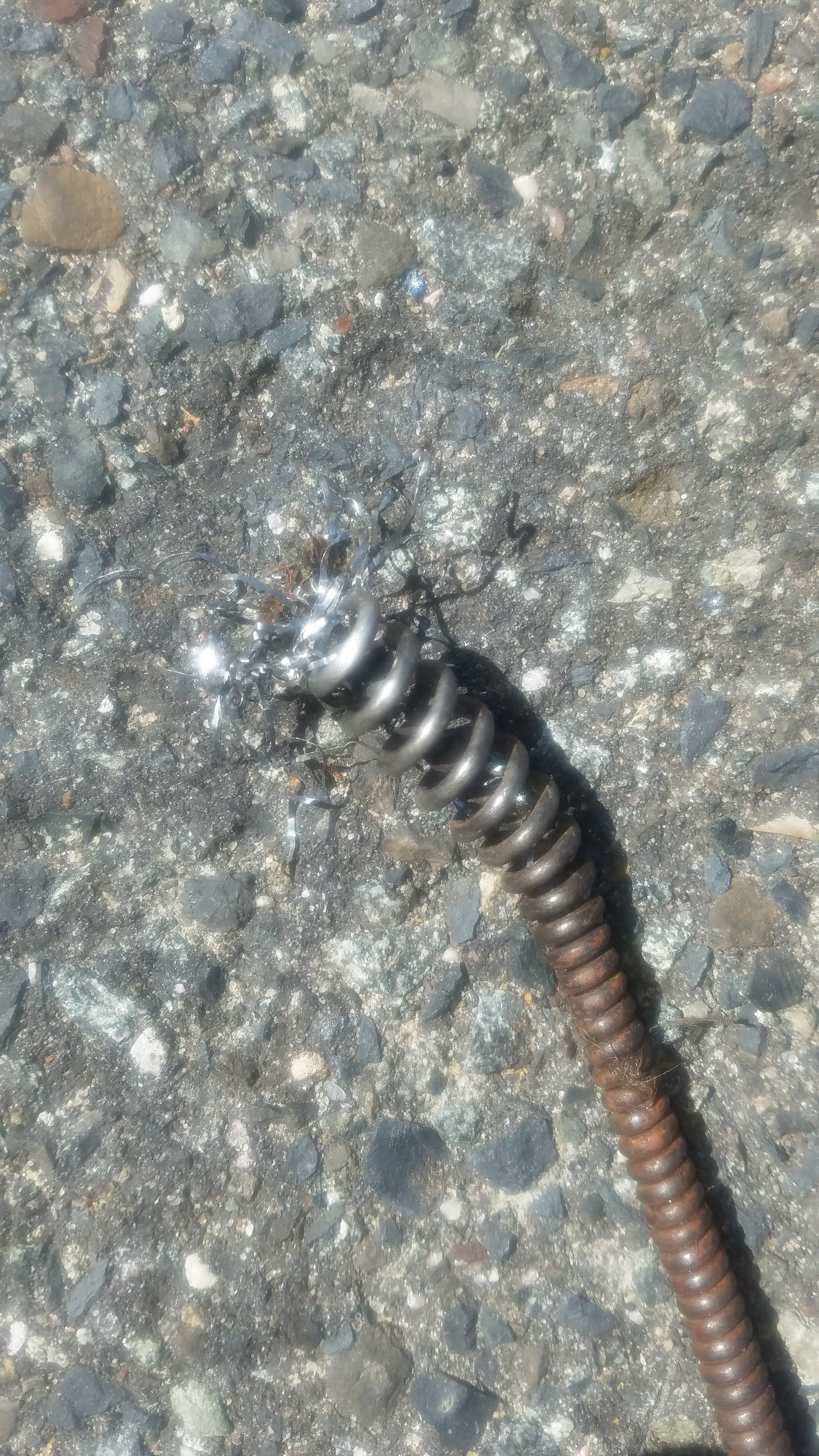 Close-up of a rusty drain snake head, coiled metal, on a gray, textured surface.