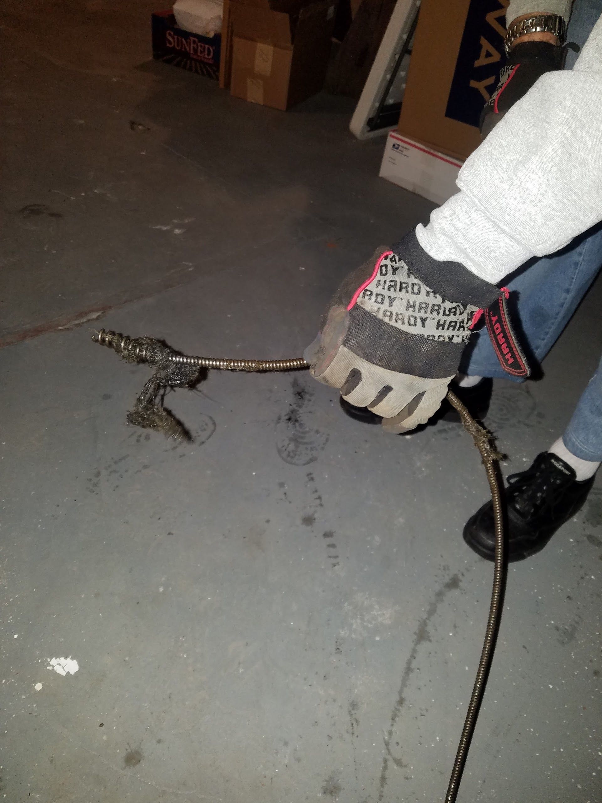 Person wearing gloves holds a metal chain, possibly an artwork, on a concrete floor.