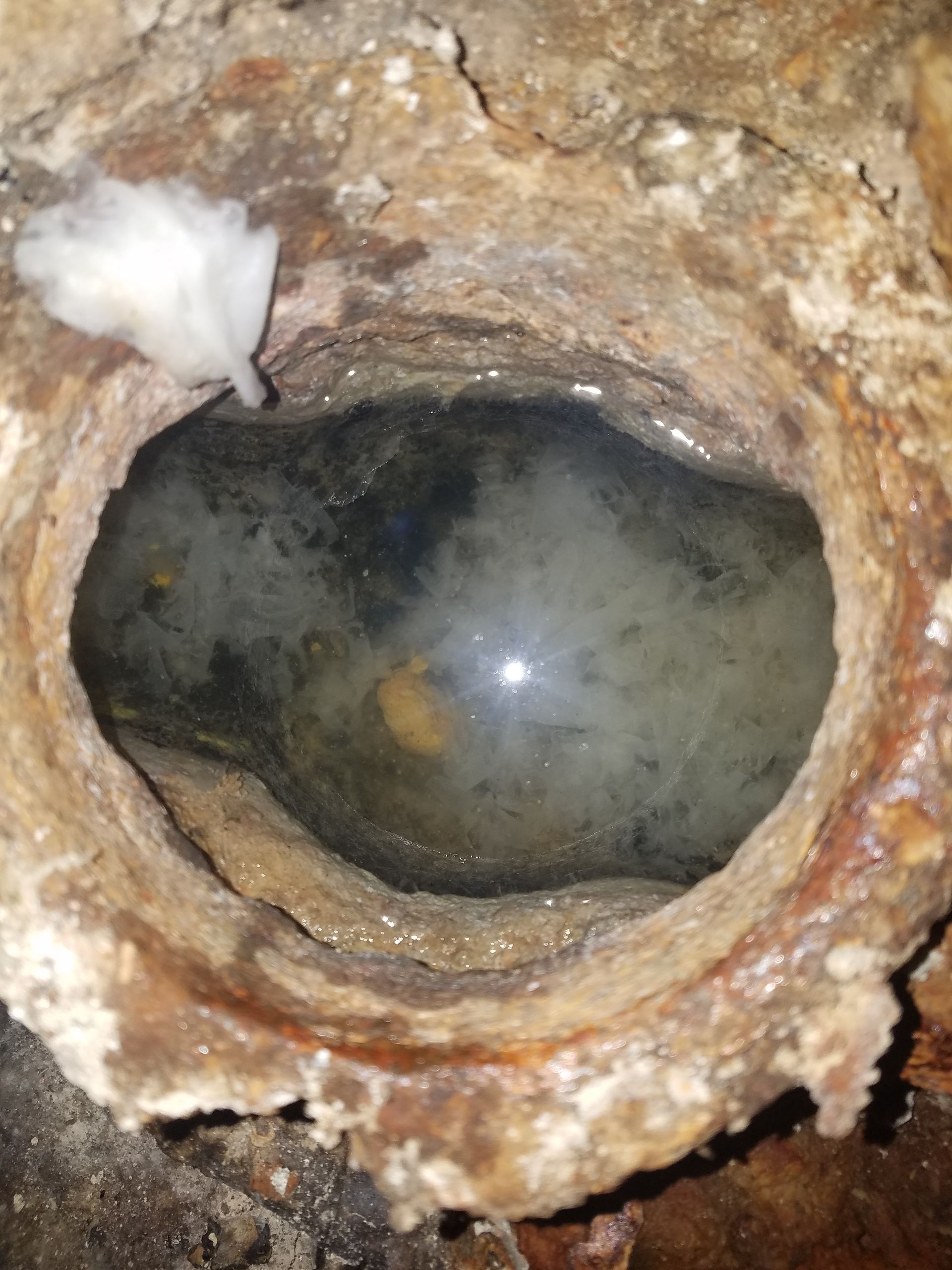 Rusty pipe interior with a partially visible, oval-shaped obstruction filled with murky liquid.