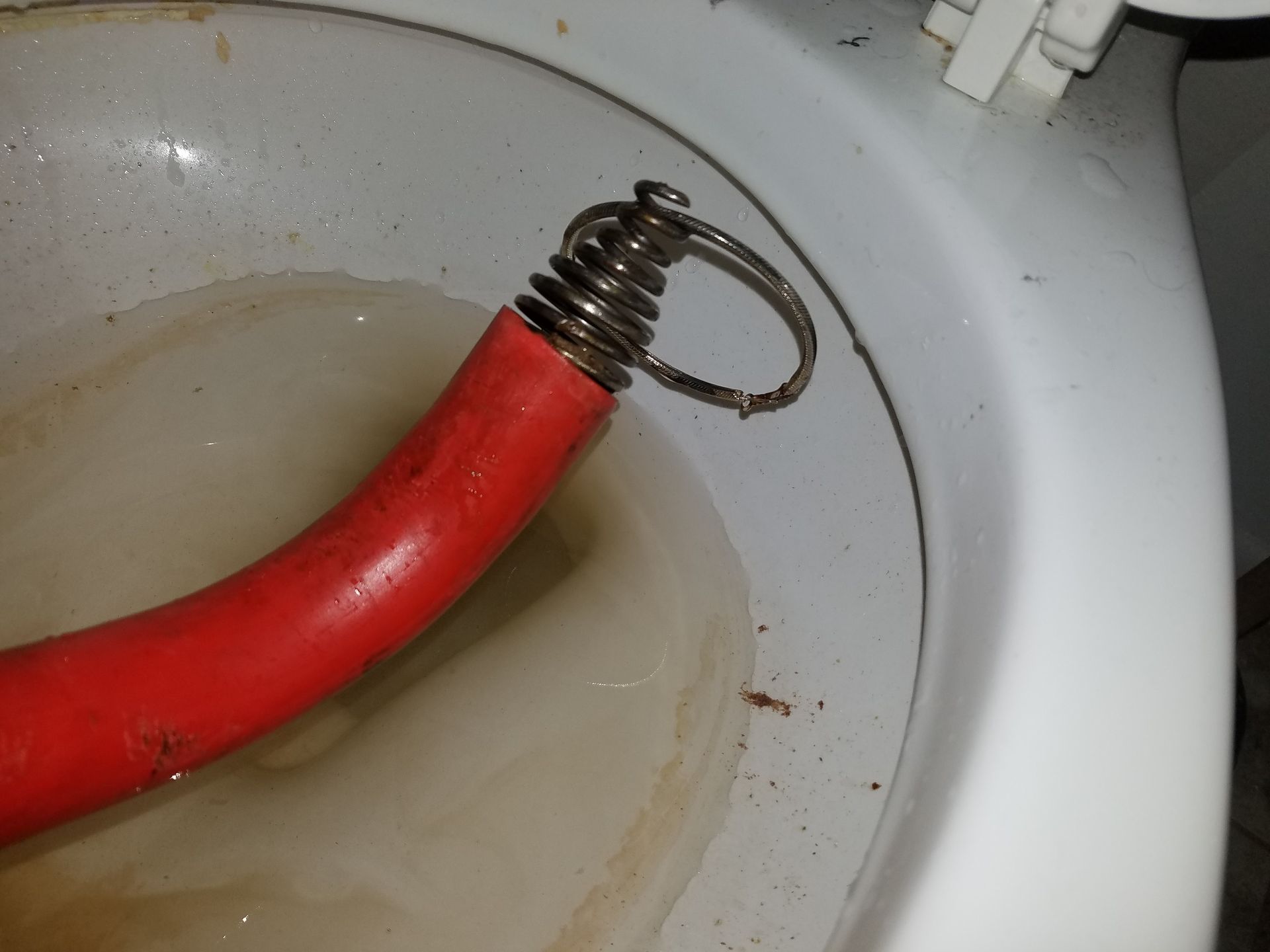 A red toilet snake tool inserted into a dirty white toilet bowl.