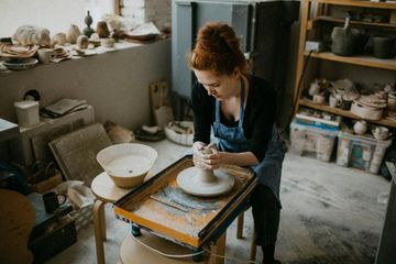 A woman is sitting at a pottery wheel making a pot.