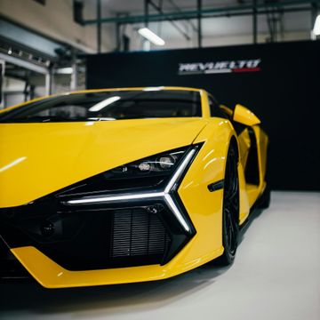 A yellow sports car is parked in front of a wall that says revolution