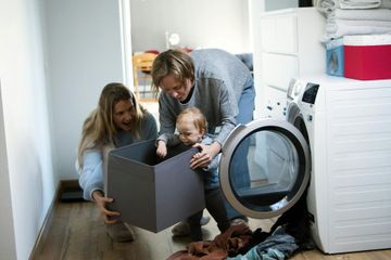 A family is playing with a box in front of a washing machine.