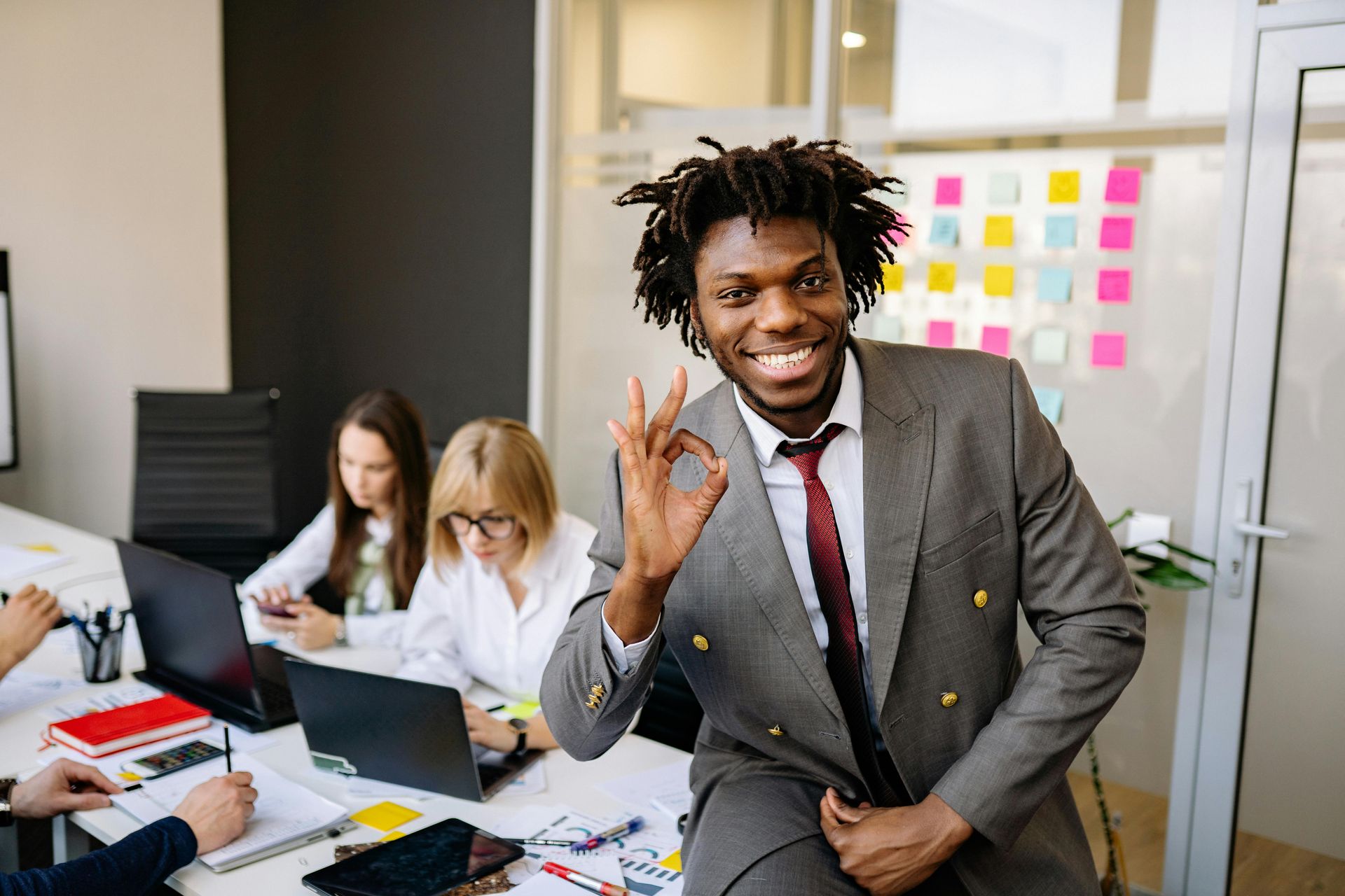 A man in a suit and tie is sitting at a table giving an ok sign.