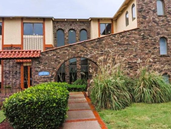Brick and stucco building with arched entryway, small garden, and path.