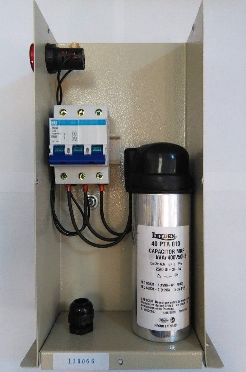 Una caja metálica montada en la pared que contiene un disyuntor y un condensador eléctrico cilíndrico.