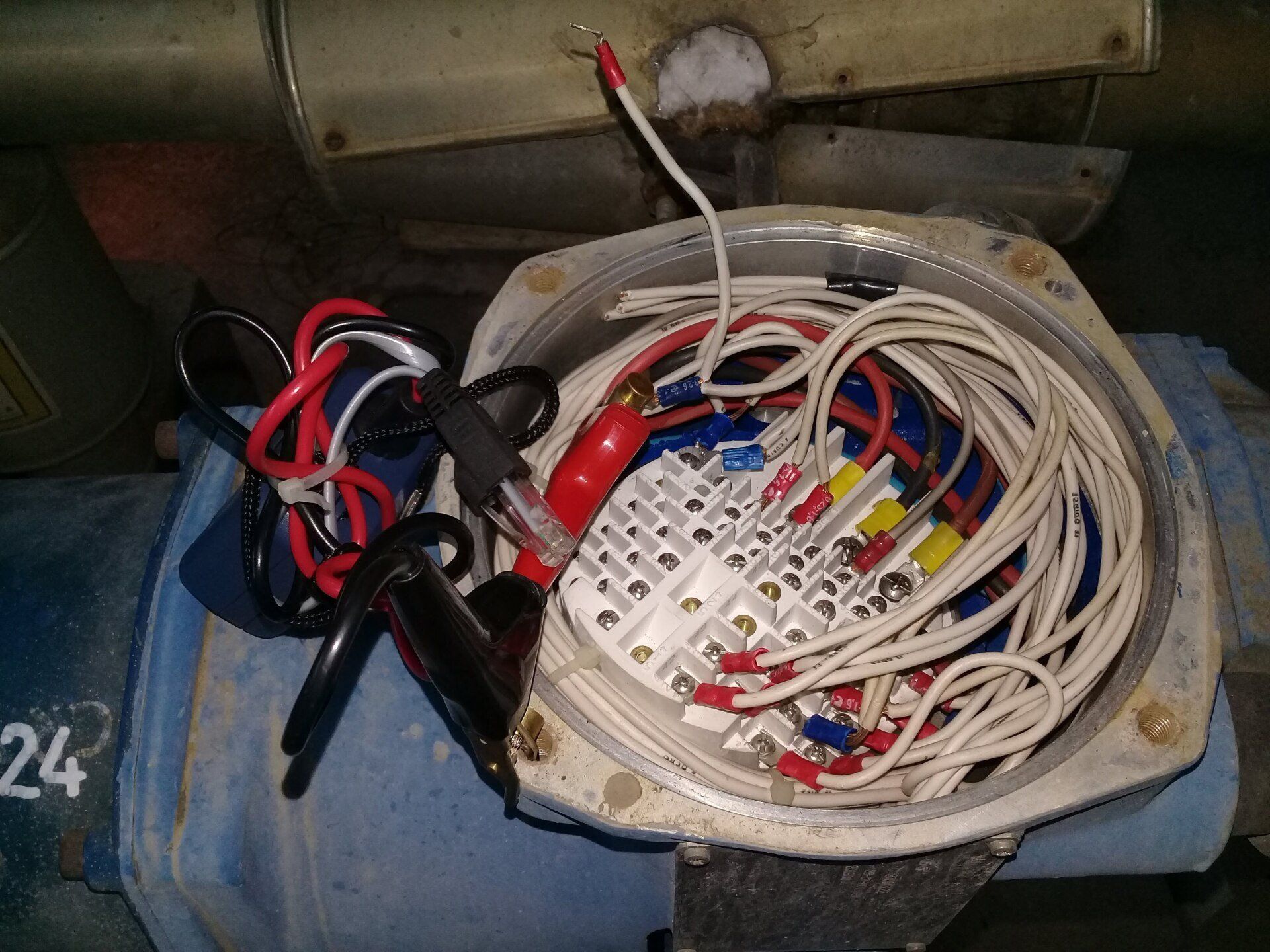Caja de conexiones eléctricas abierta en una carcasa de motor azul, que muestra un cableado complejo conectado a un bloque de terminales blanco.