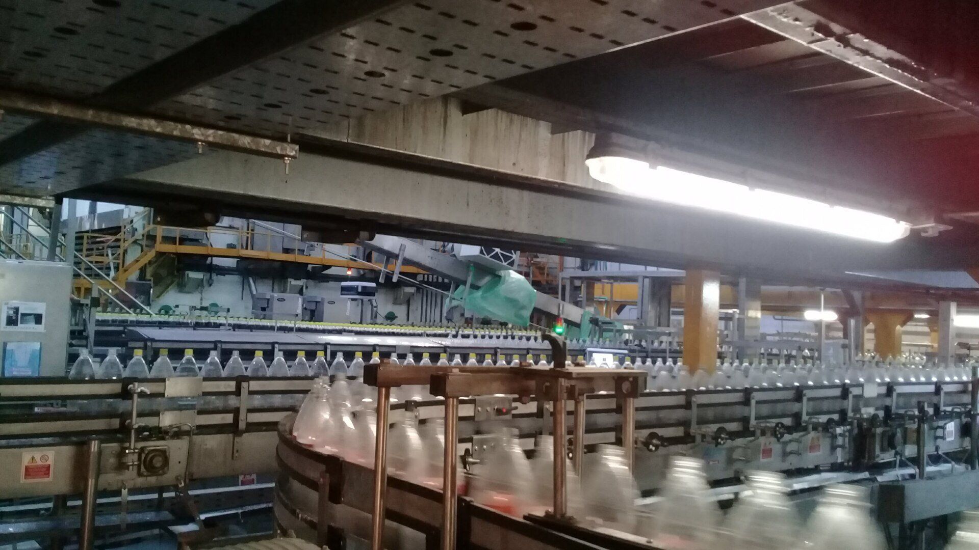 En una línea de embotellado de fábrica se observan filas de botellas transparentes que se desplazan a lo largo de una cinta transportadora bajo luces industriales.